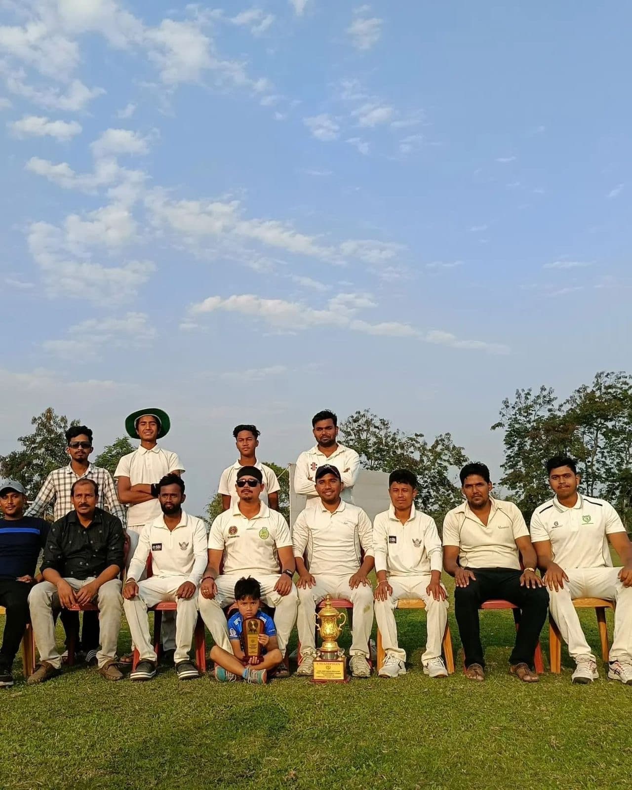 सफेद वर्दी में क्रिकेट टीम मैदान पर ट्रॉफी के साथ समूह फोटो खिंचवाते हुए।