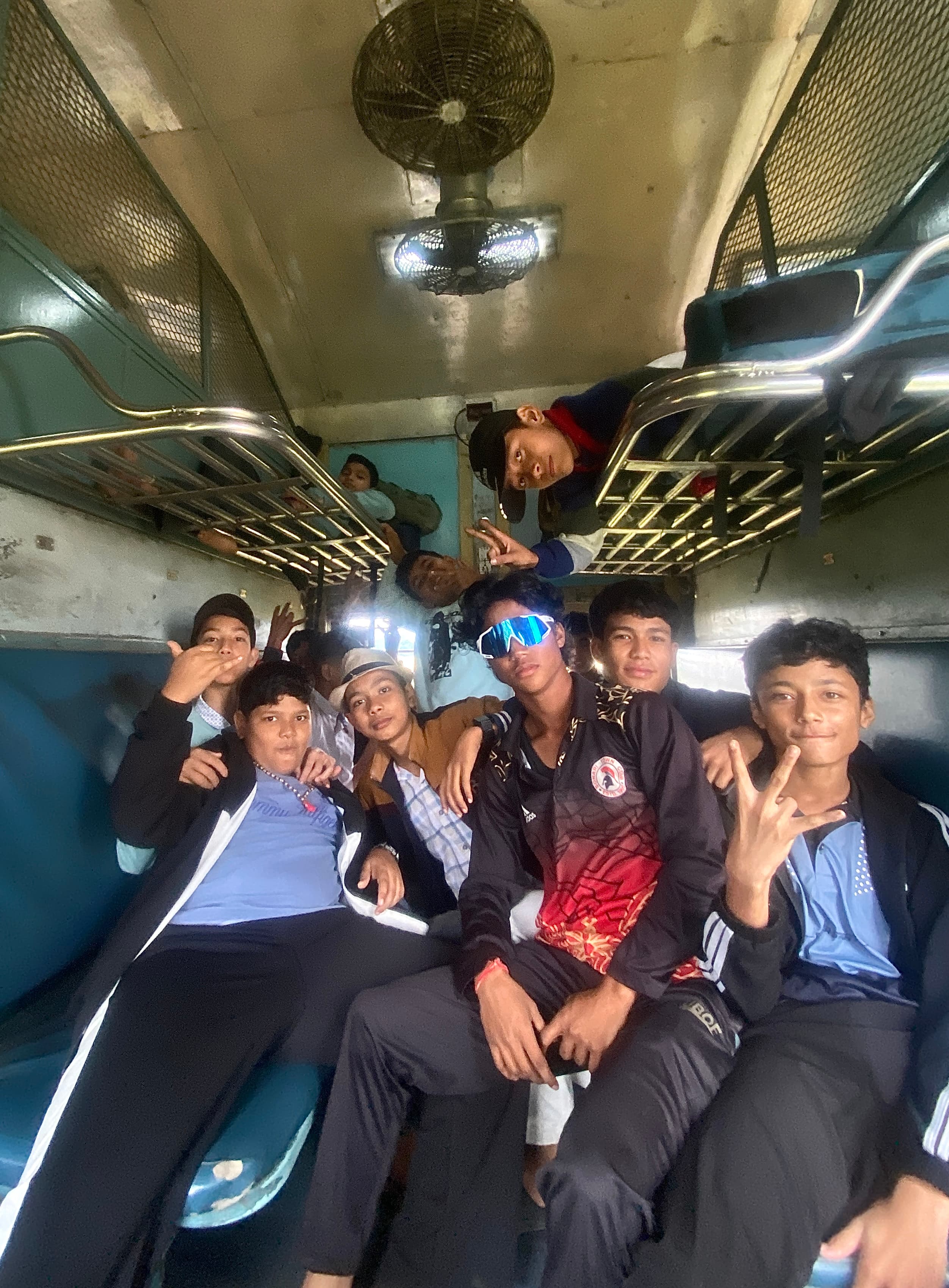 ट्रेन के डिब्बे के अंदर मुस्कुराते हुए और पोज़ देते हुए लड़कों का एक समूह।