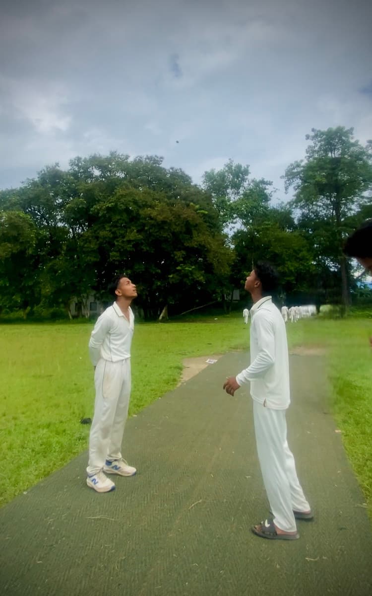 सफेद वर्दी पहने दो क्रिकेटर हरी पिच पर ऊपर आसमान की ओर देखते हुए।