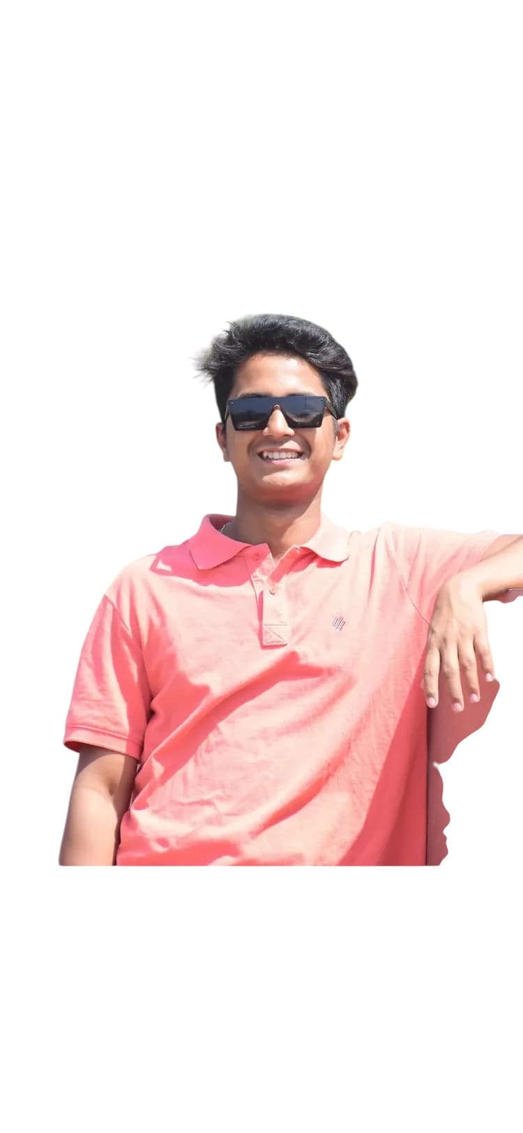 गुलाबी पोलो शर्ट और काले चश्मे पहने मुस्कुराता हुआ युवक दीवार के सहारे खड़ा है।