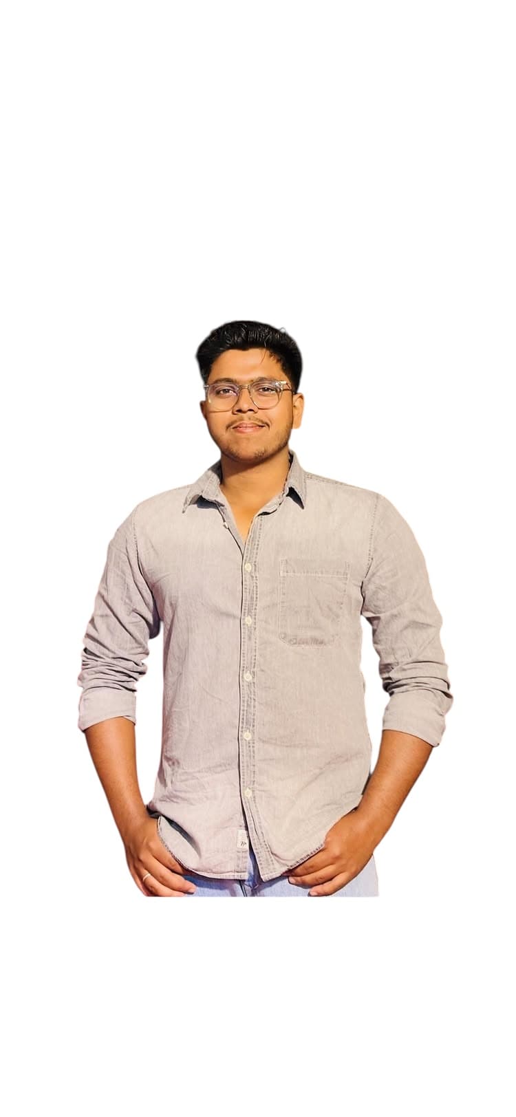 चश्मा और ग्रे शर्ट पहने मुस्कुराता हुआ युवक, सफेद पृष्ठभूमि के सामने खड़ा है।