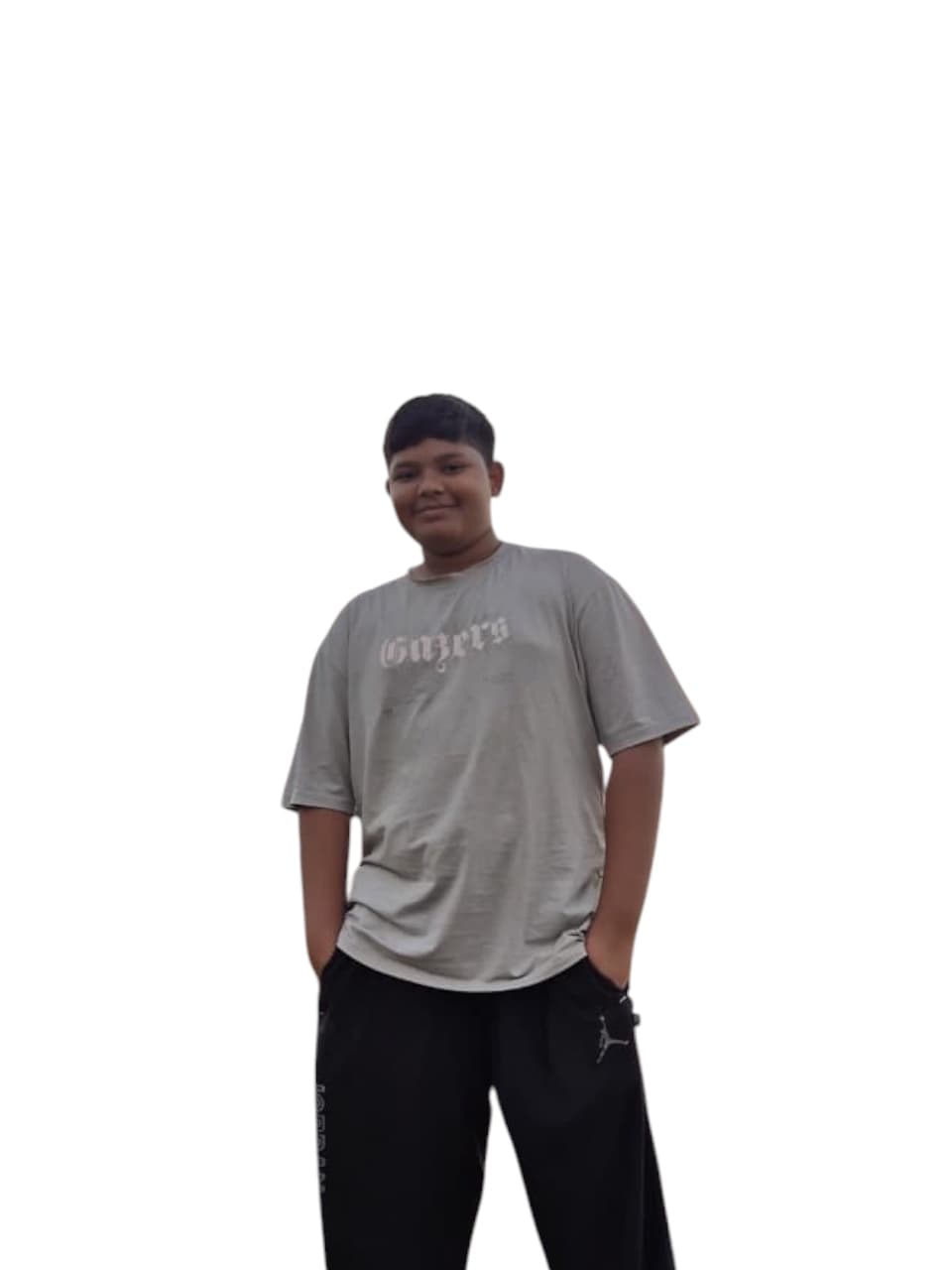 सफेद पृष्ठभूमि के सामने ग्रे टी-शर्ट और काली पैंट पहने मुस्कुराता हुआ एक युवा लड़का।